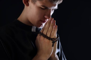 Siyah arka planda tespih çeken bir rahip, metin için yer var.