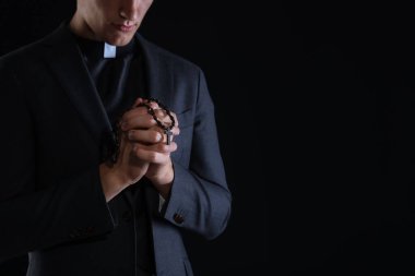 Siyah arka planda tespih çeken bir rahip, yakın plan. Metin için boşluk