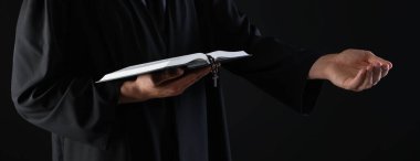 Kutsal İncil 'i olan ve siyah arka planda vaaz veren bir rahip, yakın plan.