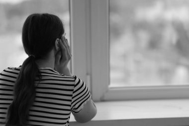 Evinin penceresinin yanında üzgün genç bir kadın, arka manzara ve mesaj için yer. Siyah ve beyaz etkisi