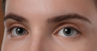 Kahverengi arka planda güzel kaşları olan genç bir kadın, yakın plan.