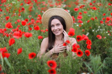 Kırmızılı gelincik çiçekleri arasında şapkalı gülümseyen kadın portresi