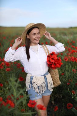 Gülen kadın şapkalı, çayırda bir torba gelincik çiçeğiyle.