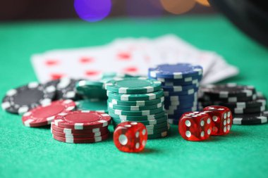 Kumarhane fişleri, zarlar ve iskambil kartları yeşil masada bulanık ışıklara karşı, yakın plan