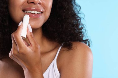 Gülümseyen kadın açık mavi arka planda dudaklarına merhem sürüyor.