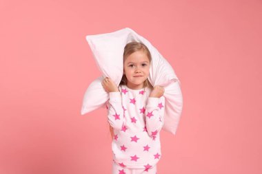 Pembe arka planda yastıklı pijamalı şirin bir kız.