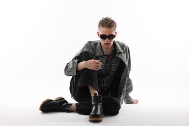 Beyaz arka planda şık ceket ve güneş gözlüğü takan yakışıklı bir genç.