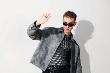 Beyaz arka planda şık ceket ve güneş gözlüğü takan yakışıklı bir genç.