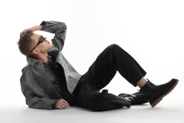 Beyaz arka planda şık ceket ve güneş gözlüğü takan yakışıklı bir genç.