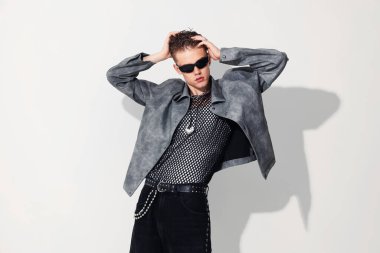 Beyaz arka planda şık ceket ve güneş gözlüğü takan yakışıklı bir genç.