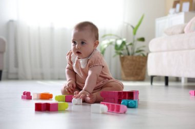 Evde yerde oyuncaklarla oynayan şirin bir bebek.