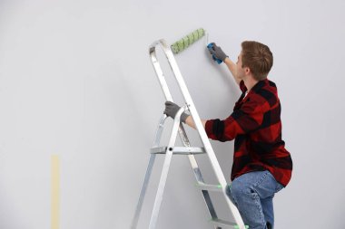Merdivendeki adam odada tekerlekli sandalyeyle duvarı boyuyor. Metin için boşluk