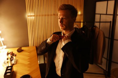 Tuvalet masasında hazırlanırken papyon ayarlayan bir adam.