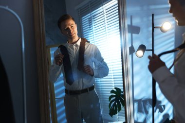 Kapalı alanda aynanın yanında kravat seçen bir adam.