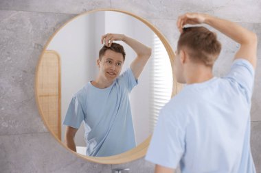 Genç adam evde aynanın yanında hazırlanıyor.