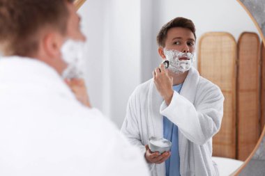 Hazırlanıyor. Genç adam evde aynanın yanında kremayla tıraş oluyor.