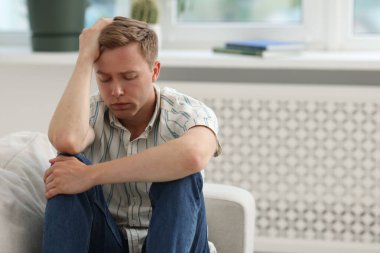 Üzgün düşünceli bir adam evdeki kanepede oturuyor, mesaj için yer var.