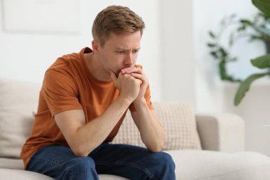 Evdeki kanepede üzgün, düşünceli bir adam.