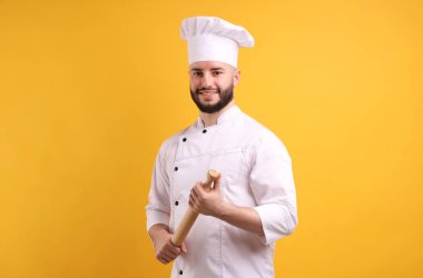 Üniformalı mutlu pastacı turuncu arka planda merdane tutuyor.