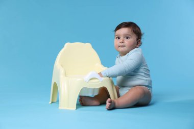 Açık mavi arka planda lazımlığın yanında oturan sevimli küçük bebek.