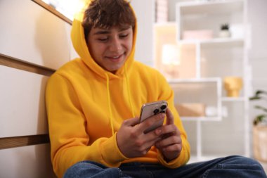 Evde akıllı telefon kullanan gülümseyen genç çocuk.