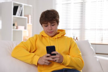 Genç çocuk evdeki kanepede akıllı telefon kullanıyor.