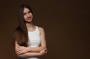 Kahverengi arka planda sağlıklı uzun saçlı güzel bir genç kızın portresi. Metin için boşluk