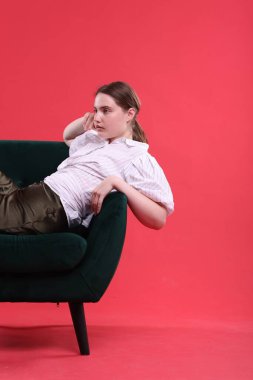 Güzel genç bayan kırmızı arka planda koltukta oturuyor.