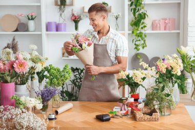 Profesyonel çiçekçi dükkandaki ahşap masada çiçek buketi yapıyor.