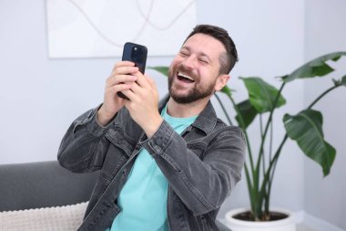 Adam içeride akıllı telefondan bir şey izlerken gülüyor.