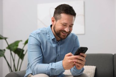 Adam evde akıllı telefondan bir şey izlerken gülüyor.