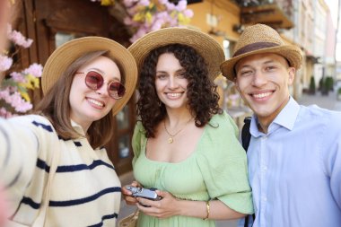 Hasır şapkalı turistler şehir sokaklarında selfie çekiyorlar.