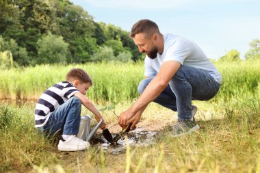 Baba ve oğlu dışarıda toprağa ağaç dikiyorlar.