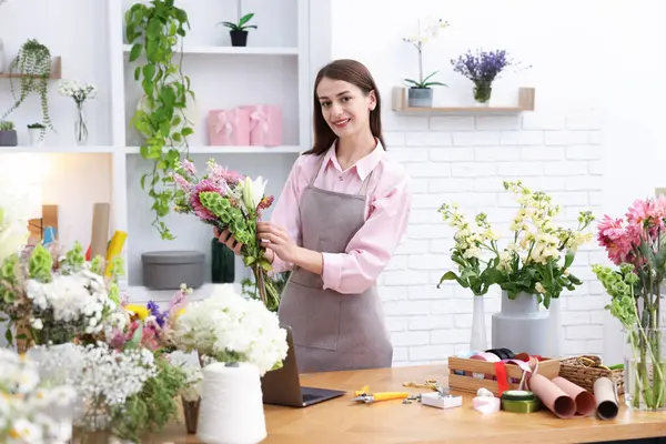 Profesyonel çiçekçi dükkandaki ahşap masada çiçek buketi yapıyor.