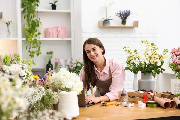 Dükkandaki tahta masada dizüstü bilgisayarla çalışan profesyonel bir çiçekçi.