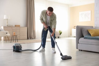 Evin zeminini elektrikli süpürgeyle temizleyen adam.