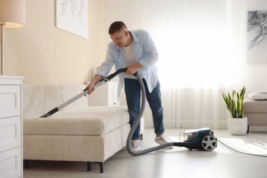 Evdeki elektrikli süpürgeyle kanepeyi temizleyen adam.