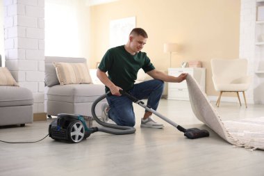 Evin zeminini elektrikli süpürgeyle temizleyen adam.
