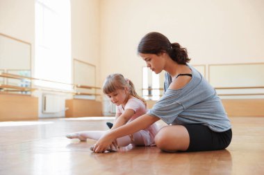 Dans dersinde küçük kızın yere uzanmasına yardım eden bale öğretmeni.