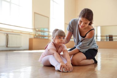 Gülümseyen bale öğretmeni dans dersinde küçük kızın esnemesine yardım ediyor.