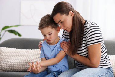 Annesi evdeki kanepede üzgün oğlunu destekleyip kucaklıyor.