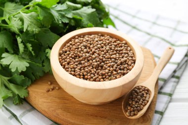 Kişniş tohumu ve taze kişniş beyaz ahşap masada, yakın plan.