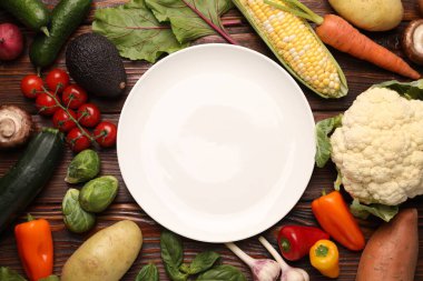 Sağlıklı vejetaryen yemekleri. Tahta masanın üzerinde farklı ürünlerle çevrili boş bir tabak.