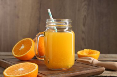 Mason kavanozunda lezzetli portakal suyu, ahşap masada taze meyve suyu ve meyve sıkacağı.