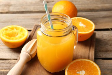 Mason kavanozunda lezzetli portakal suyu, ahşap masada taze meyve suyu ve meyve sıkacağı, yakın plan.