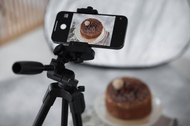 Stüdyoda akıllı telefonla çikolatalı pasta çekmek, seçici odaklanma. Profesyonel yemek fotoğrafçılığı.
