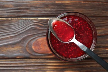 Cam kavanozda tatlı ahududu reçeli ve tahta masada kaşık, üst manzara. Metin için boşluk