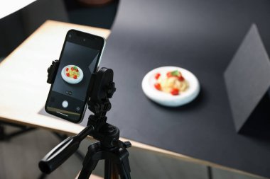 Stüdyoda akıllı telefonla lezzetli makarna çekmek, ekrana odaklanmak. Profesyonel yemek fotoğrafçılığı.