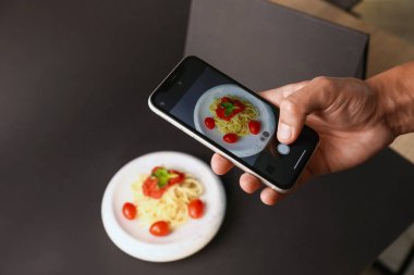 Adam stüdyoda akıllı telefonlu makarna fotoğrafı çekiyor, yakın plan. Profesyonel yemek fotoğrafçılığı.