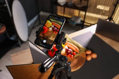 Stüdyoda akıllı telefonla sebze çekmek, ekrana odaklanmak. Profesyonel yemek fotoğrafçılığı.